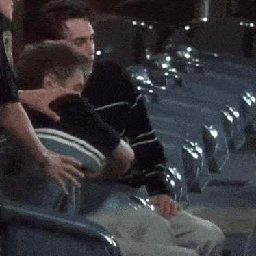 a man in a black and white striped shirt is sitting next to another man in a blue chair