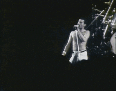 a shirtless man sings into a microphone on a stage