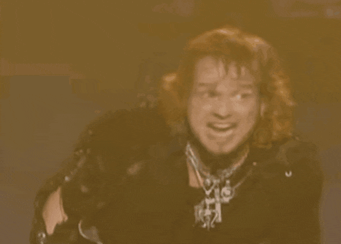 a man with long red hair is wearing a black jacket and a necklace