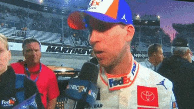 a man wearing a fedex hat talks into a microphone in front of a martinsville sign