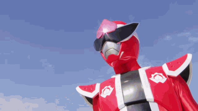 a close up of a red superhero with a blue sky behind him