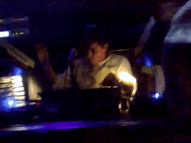 a man playing drums in a dark room with a mask in the background