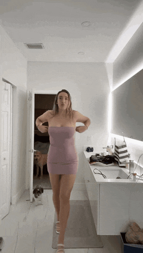 a woman in a pink dress is standing in a bathroom next to a dog