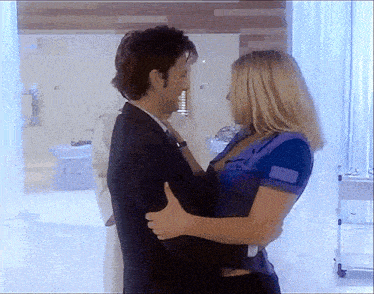 a man in a suit and tie holds a woman in a blue shirt