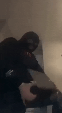 a man in a ski mask is standing in a room holding a laptop .