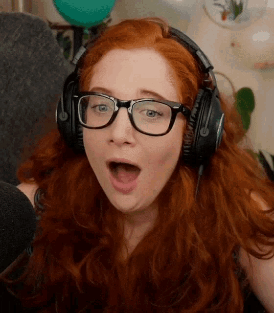 a woman with red hair wearing glasses and headphones making a surprised face