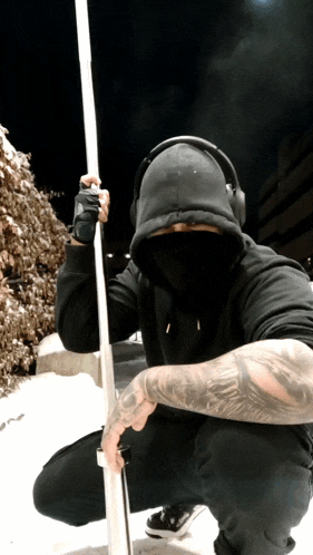 a man wearing headphones and a black hoodie holds a pole in front of his face