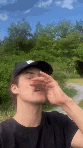 a young man wearing a baseball cap is covering his face with his hand