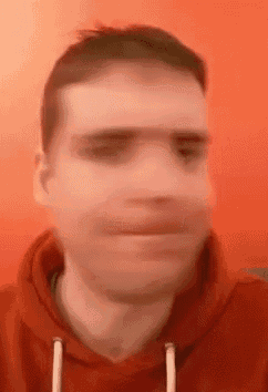 a blurry picture of a man in a red hoodie making a funny face .