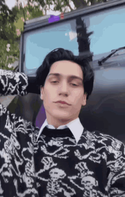 a young man wearing a black and white sweater with skulls and crossbones is standing in front of a black jeep .