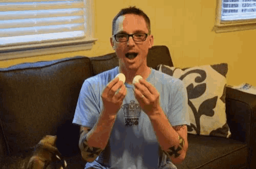 a man sitting on a couch holding two eggs in his hands and wearing a shirt that says ucsd 2014