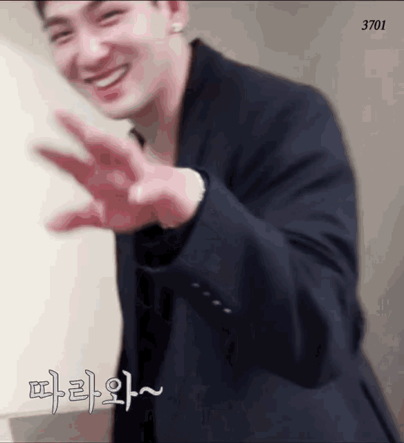 a man in a suit is smiling and waving his hand while wearing earrings .
