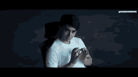 a young man in a white shirt is sitting in a chair and clapping his hands .