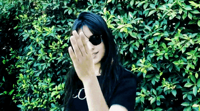 a woman wearing sunglasses and a patch on her eye is standing in front of a bush