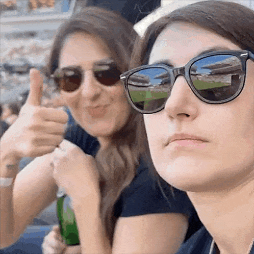 two women wearing sunglasses giving a thumbs up