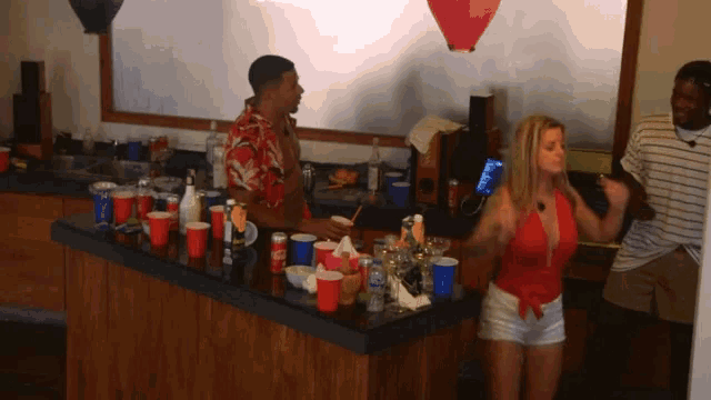 a woman in a red top is dancing in front of a bar full of red cups
