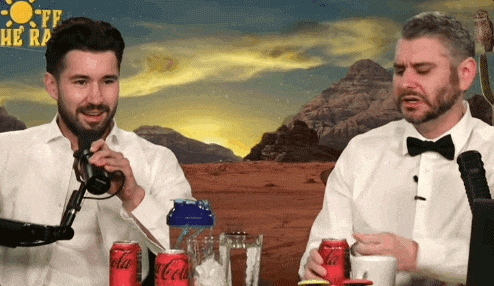 two men are sitting at a table with coca cola cans