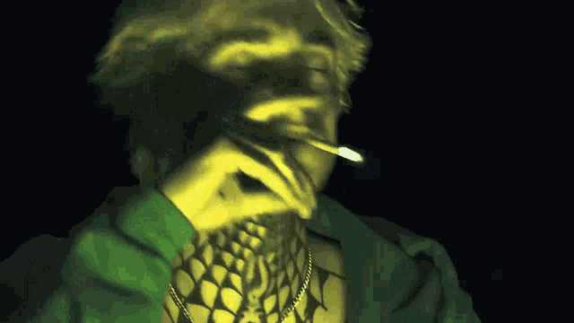 a man in a green jacket is smoking a cigarette in the dark
