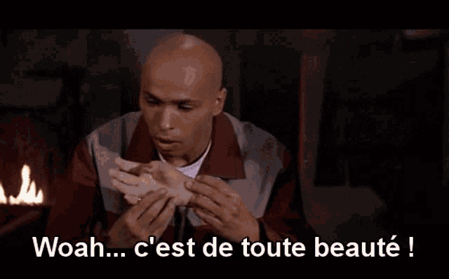 a bald man in a red and grey jacket is holding a white object and says woah c'est de toute beaute !