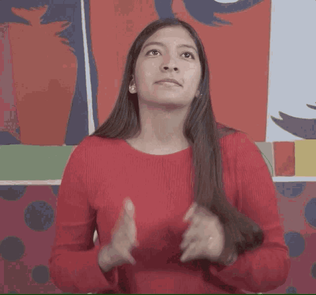 a woman in a red sweater is clapping her hands in front of a polka dot wall .