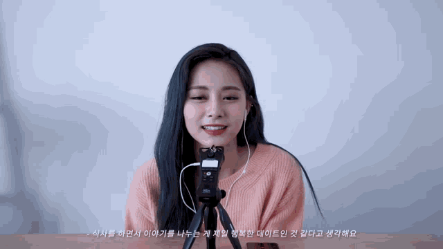 a woman wearing headphones and a pink sweater stands in front of a camera