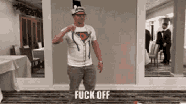 a man wearing a superman shirt is dancing in a room with the words fuck off written on the floor