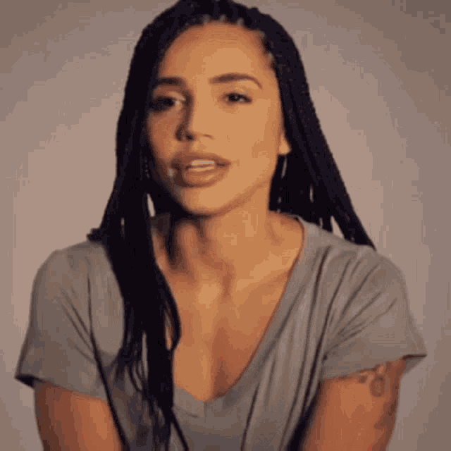 a woman with braids and a tattoo on her arm is wearing a gray shirt .