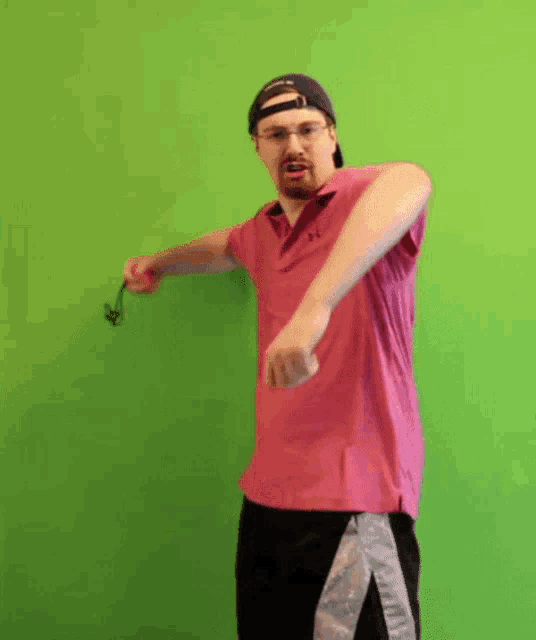 a man in a pink under armour shirt is standing in front of a green wall