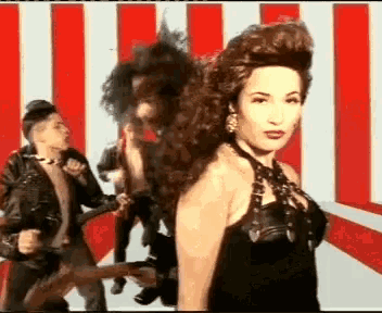 a woman in a black dress is standing in front of a man in a leather jacket .