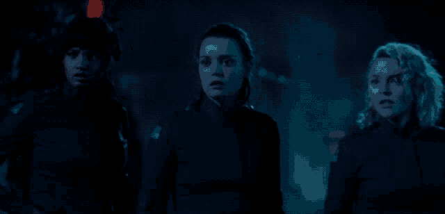 three women are standing next to each other in a dark room with a blue light behind them
