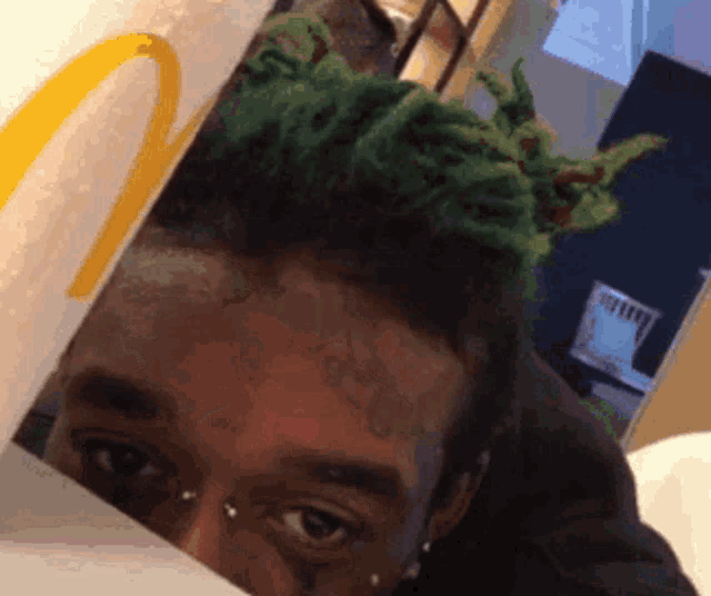 a man with green hair is peeking out from behind a mcdonalds bag