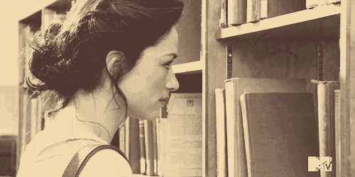a woman is looking at books in a library with a mtv logo in the corner