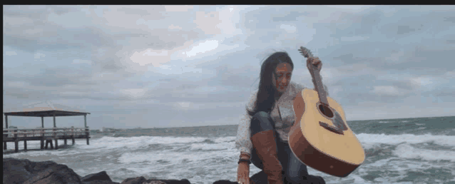a woman sits on a rock holding an acoustic guitar