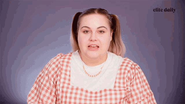 a woman in a plaid shirt is making a face in front of an elite daily logo