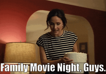 a woman is holding a cake and a bucket of popcorn and the caption says family movie night guys