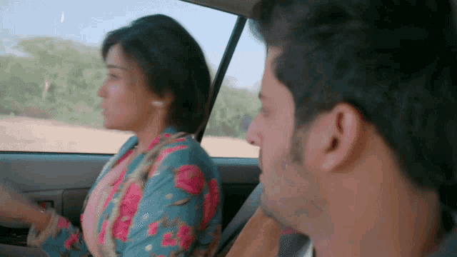 a man and a woman are in a car and the woman is wearing a floral jacket