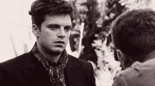 a man in a suit and scarf is standing next to another man in a black and white photo .