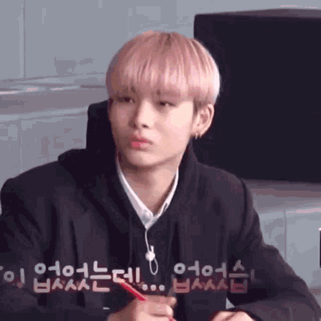 a young man with pink hair is sitting at a desk in a classroom holding a pencil .