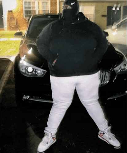 a man wearing a nike hat stands in front of a black car