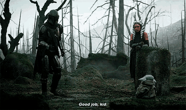 a man and a woman are standing in a forest talking to a baby yoda .