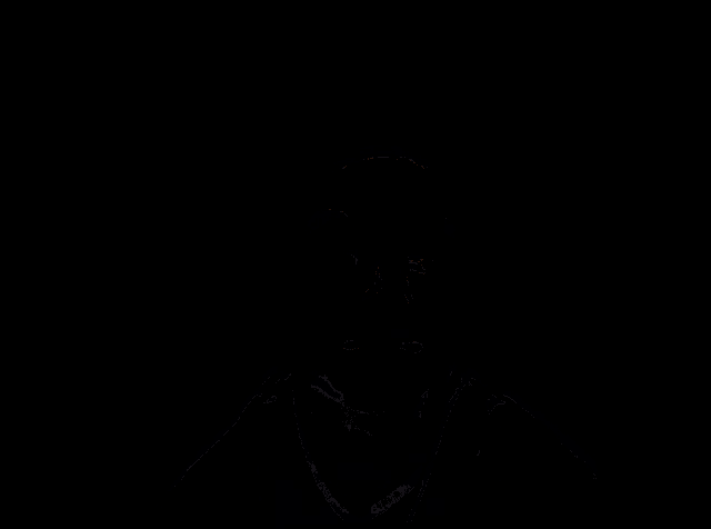 a man in a white nike shirt sticks his tongue out in a dark room