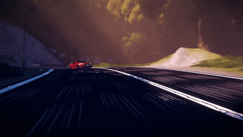 a red car is driving down a dark road with trees in the background