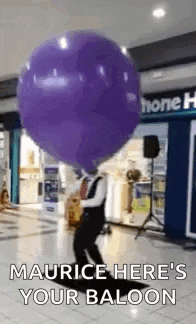 a man is blowing up a large purple balloon in a shopping mall .