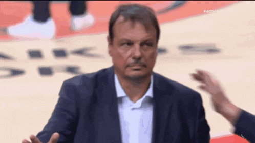 a man in a suit and white shirt is sitting on a basketball court