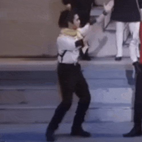 a man in a white shirt and black pants is dancing on a stage with a group of people .