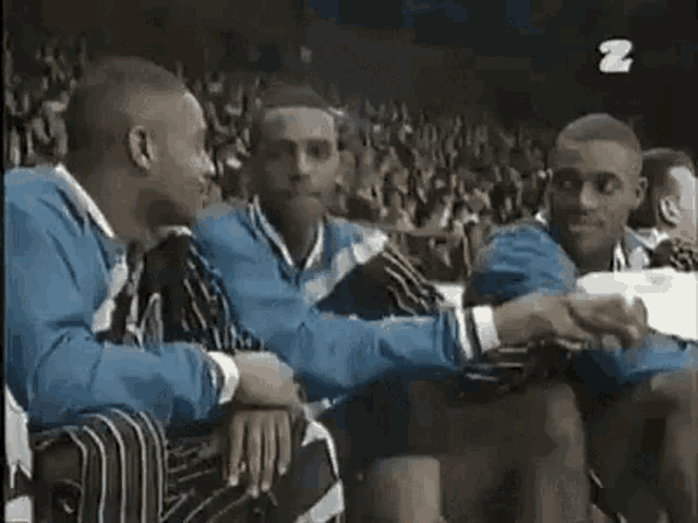 a group of men are sitting next to each other in a stadium and shaking hands .