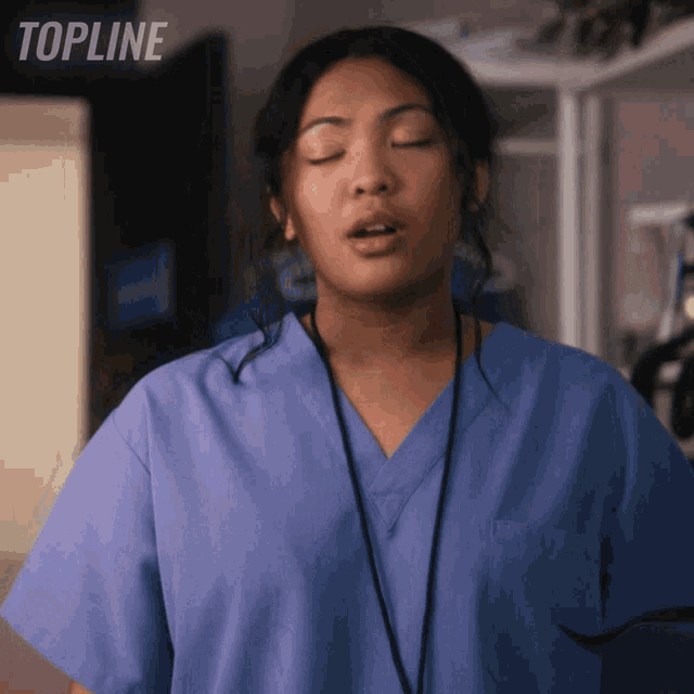 a woman in a blue scrub is standing in front of a sign that reads topline