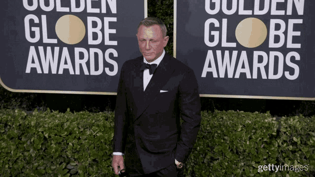 a man in a tuxedo is standing in front of a sign that says golden globe awards
