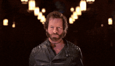 a man with a beard is wearing a leather jacket with studs