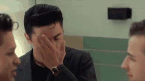 a man in a suit and tie is covering his face with his hand while talking to two other men .